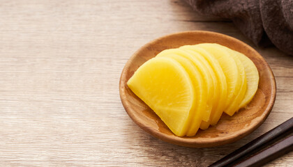 Korean yellow pickled radish or Danmuji side dish in wood bowl on wooden table background          ...