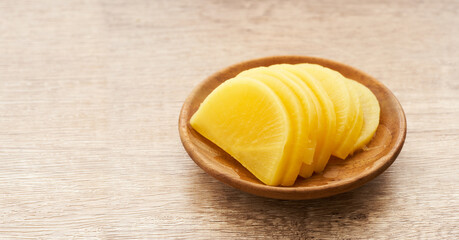 Korean yellow pickled radish or Danmuji side dish in wood bowl on wooden table background                                                             