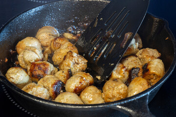 Frying pork sausage meat balls, with olive oil, in a cast iron frying pan, on an electric hob stove