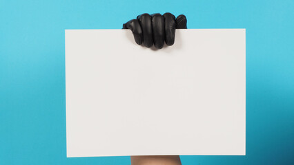 Hand is holding the A4 paper and wear black latex glove on blue background.