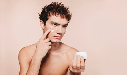 Close up shot of attractive young man with healthy skin, applies cream moisturizer for anti wrinkle...