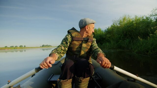 Fifty-year-old fisherman on an inflatable boat rowing on the lake in the morning