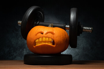 Carved Halloween pumpkin lifting a heavy barbell dumbbell. Weightlifting carving idea with...