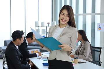 Portrait of Asian businesswoman standing and using paper document with business people meeting and talking in the room background