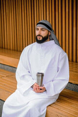 Young arabian man sitting on a wooden bench with metal