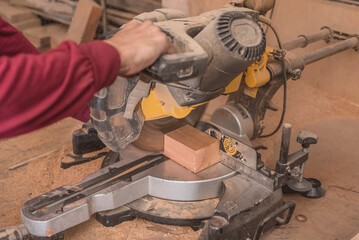 A furniture maker uses a miter saw to cut a block of wood. Cutting lumber at a woodworking shop.