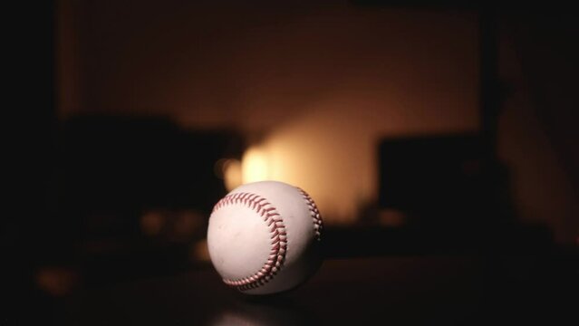 The baseball rolls slowly on the table, against the backdrop of orange lights.