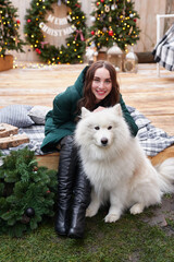 Young woman on background of Christmas tree with white samoyed dog outdoors. Yard decoration for New Year