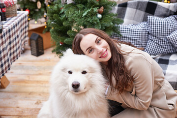 Young woman on background of Christmas tree with white samoyed dog outdoors. Yard decoration for New Year