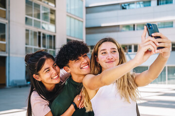 Cheerful diverse friends taking selfie on smartphone on city street