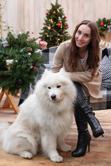 Young woman on background of Christmas tree with white samoyed dog outdoors. Yard decoration for New Year