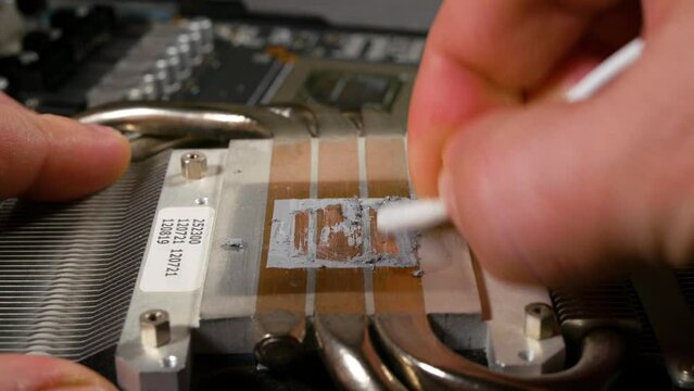 The computer master repairs the video card. Replacing the thermal paste in the video card. The master removes the old, dried thermal paste from the cooling radiator. Close-up, selective focus.