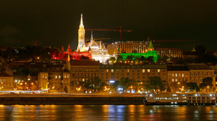 Fototapeta na wymiar Budapest by night with illuminated Matthias Church and Fisherman's Bastion. On national holidays national flag colors are used: red, white, green.