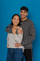 Young smiling stylish guy hugging his happy beautiful asian girlfriend