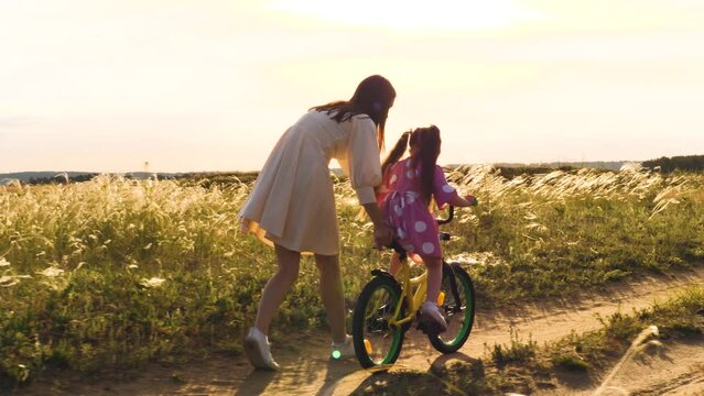 mother teaches little child daughter ride bike park sunset. cycling kid with parent outdoors. happy family. mother daughter play with bicycle nature. happy family concept. chidhood dream. weekend.