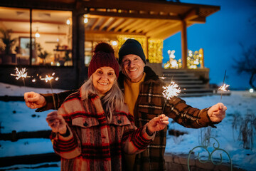 Fototapeta na wymiar Happy senior couple celebrating new year with sparklers, enjoying winter evening.