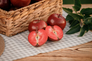 Fresh ripe red apples in the basket on wooden table with natural orchard background. Vegetarian fruit composition. Harvesting concept