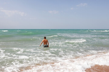 man enters the sea to bathe. Moderate sea waves, sandy beach, sea foam