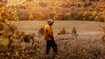 a man in a yellow jacket walks through the autumn forest