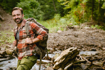 Fototapeta premium Young white man with backpack smiling while hiking in forest