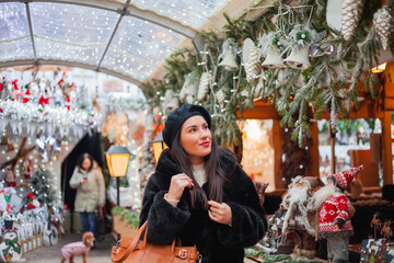 Naklejka premium Beautiful dark-haired young woman in an eco fur coat walks around the city and does Christmas shopping. New Year holidays. Present. Holidays. Winter.