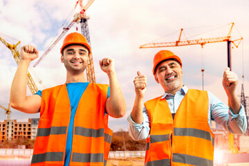 Older construction supervisor with younger worker helper at construction site. Managers wearing...