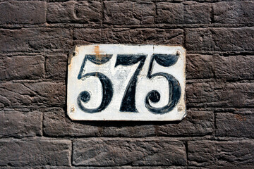 house number five hundred and seventy five. Hand painted on a white plate.