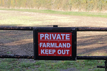 A red sign on a gate in the countryside reads Private Farmland, Keep Out.