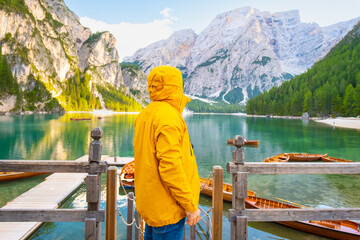Tourist with hiking outfit enjoying the amazing view of alpine lake Braies with boats and Dolomites. Man in a yellow sport jacket looking into the distance 