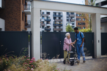 Caregiver walking with senior woman client in front of nurishing home.