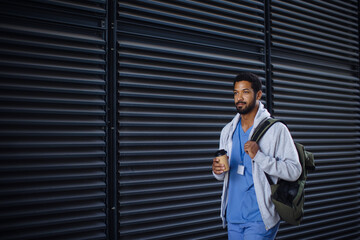 Young multiracial man working as nurse coming back from work and holding cup of coffee.