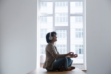 middle aged woman wearing headphones relaxed and does meditation sitting on a desk in the office....