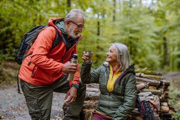 Senior couple having break during hiking in autumn forest.