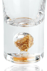 Cropped close-up shot of an empty shot glass with gold flakes at the bottom. A shot glass with a thick base is isolated on a white background. Front view.