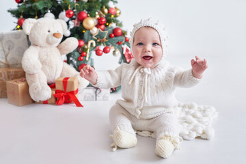 Santa baby. Christmas tree background. Happy New Year! Child in knitted suit