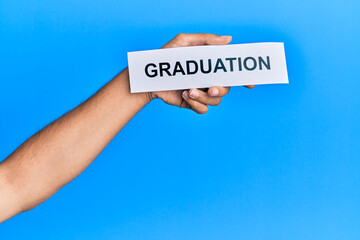 Hand of caucasian man holding paper with graduation word over isolated blue background