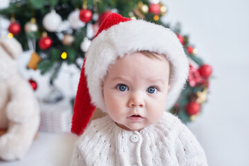 Santa baby. Christmas tree background. Happy New Year! Child in Santa's hat.