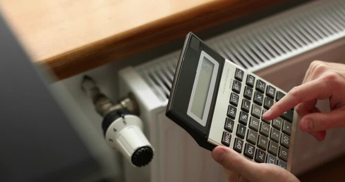hand holding a calculator near radiator, temperature regulation in house
