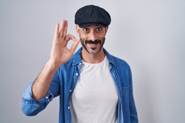 Hispanic man with beard standing over isolated background smiling positive doing ok sign with hand and fingers. successful expression.