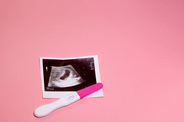 Photo of ultrasound and pregnancy test on a pastel pink background. Positive pregnancy test
