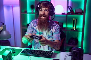 Young redhead man streamer playing video game using joystick at gaming room