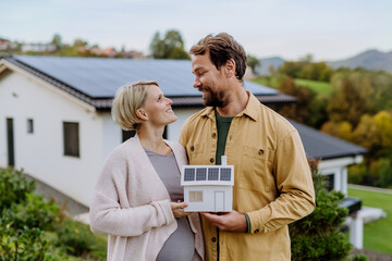 Close up of happy couple holding paper model of house with solar panels. Alternative energy, saving...