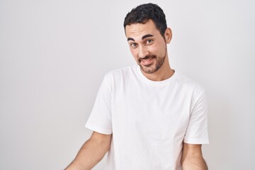 Obraz premium Handsome hispanic man standing over white background smiling cheerful with open arms as friendly welcome, positive and confident greetings