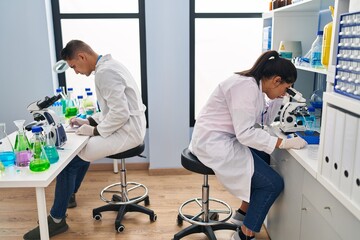 Fototapeta premium Man and woman scientists partners using microscope working at laboratory