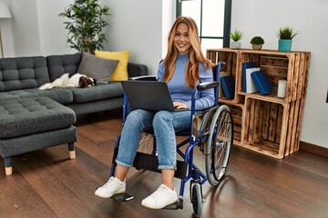 Young caucasian woman using laptop sitting on wheelchair at home