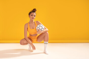 Attractive female brunette girl in fashionable sportswear and stockings posing with football ball ,...