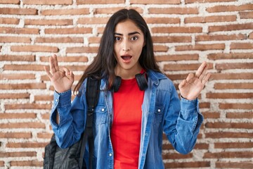 Young teenager girl wearing student backpack doing relax sign afraid and shocked with surprise and amazed expression, fear and excited face.