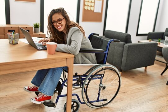Young beautiful hispanic woman business worker using laptop sitting on wheelchair at office