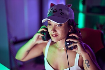 Young beautiful hispanic woman streamer holding headphones at gaming room