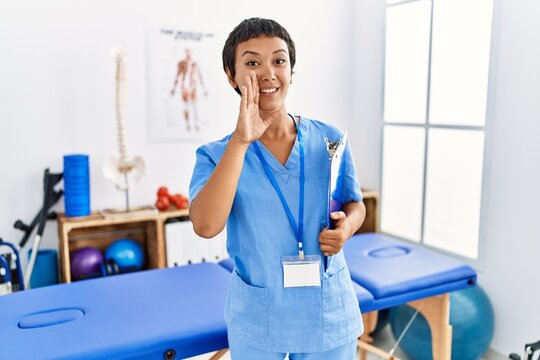 Young Hispanic Woman With Short Hair Working At Pain Recovery Clinic Hand On Mouth Telling Secret Rumor, Whispering Malicious Talk Conversation